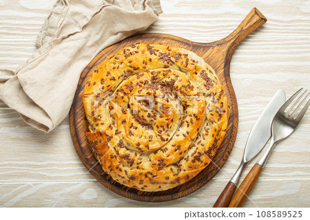 Burek made of filo dough with filling on cutting board, white wooden rustic background top view. Traditional savoury spiral pie of Balkans, Middle East and Central Asia 108589525