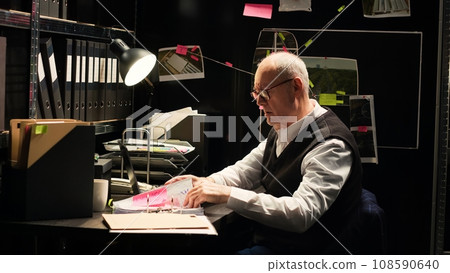 Senior detective read classified records in incident room, trying to solve crime and uncover hidden clues. Man investigator analyzing witness statements and forensic evidence reports. Senior detective read classified records in incident room, trying to solve crime and uncover hidden clues. Man investigator analyzing witness statements and forensic evidence reports. 108590640