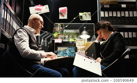 Agents examine surveillance footage and classified documents, reading confidential police records to piece the puzzle. Team of private inspectors evaluate forensic evidence reports. Tripod shot. Agents examine surveillance footage and classified documents, reading confidential police records to piece the puzzle. Team of private inspectors evaluate forensic evidence reports. Tripod shot. 108590649