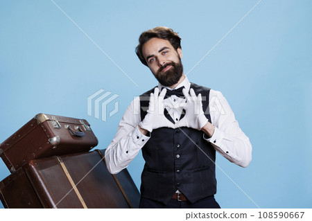 Hotel porter doing heart shape sign in studio and displaying romantic emotions, professional tourism occupation. Young man being sweet and presenting love romance symbol on camera. Hotel porter doing heart shape sign in studio and displaying romantic emotions, professional tourism occupation. Young man being sweet and presenting love romance symbol on camera. 108590667