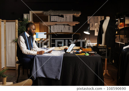 Dressmaker looking over handdrawn sketches, trying to pick best design for important event dress comissioned by rich businesswoman. Fashion designer working on bespoken garments in atelier studio 108590690