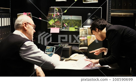 Experts team undertaking investigation with incriminating proof in incident room, examining police case files. Inspector working with detective to carry out investigatory law services. Experts team undertaking investigation with incriminating proof in incident room, examining police case files. Inspector working with detective to carry out investigatory law services. 108590699