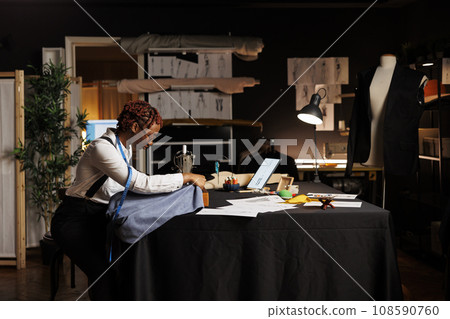 African american seamstress using industrial sew machine to do creative embroidery on piece of fabric to be used on upcoming bespoke fashion collection. Expert tailor working on sartorial collection 108590760