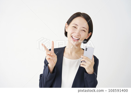 Middle-aged business woman holding a smartphone and making a peace sign, white background 108591400
