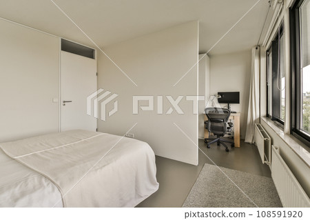 a bedroom with a bed, desk and television set in the corner next to the window that looks out onto the street 108591920