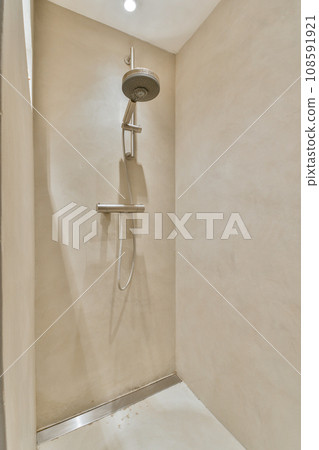 a shower in the corner of a room with beige walls and white tiles on the floor, there is a light coming from above 108591921