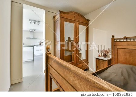a bedroom with a bed, dresser and mirror on the wall in front of the door that leads to another room a bedroom with a bed, dresser and mirror on the wall in front of the door that leads to another room 108591925