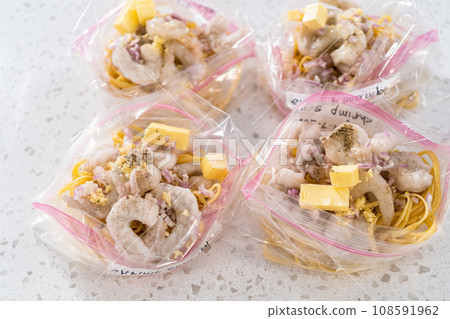 Packaging homemade frozen shrimp scampi meal prep into plastic resealable bags. Packaging homemade frozen shrimp scampi meal prep into plastic resealable bags. 108591962