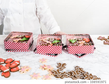 Packaging a homemade variety of fudge and gingerbread cookies for Christmas food gifts into tin boxes. 108591971