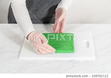 Cutting green fudge with a large kitchen knife into square pieces on a white cutting board. 108592122
