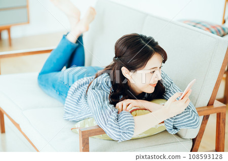 A woman operating a smartphone on the sofa. 108593128