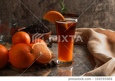Iced Americano black coffee with lower layer orange juice in the glass. Rosemary with cinnamon on top. citrus fruits and coffee beans background. Coffee and orange juice concept. Iced Americano black coffee with lower layer orange juice in the glass. Rosemary with cinnamon on top. citrus fruits and coffee beans background. Coffee and orange juice concept. 108593868