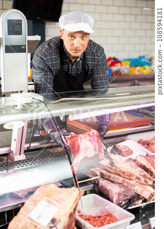 Smiling male butcher offering to sell big piece of beef in butcher shop 108594181