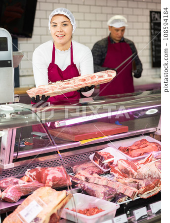 Young female butcher showing raw beef ribs at counter Young female butcher showing raw beef ribs at counter 108594184