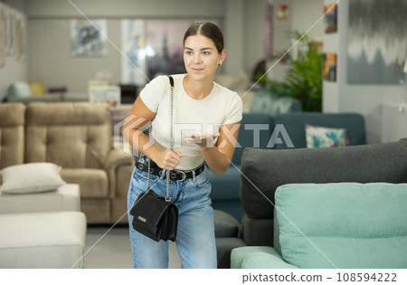 Smiling young girl looking for pieces of furniture in showroom Smiling young girl looking for pieces of furniture in showroom 108594222