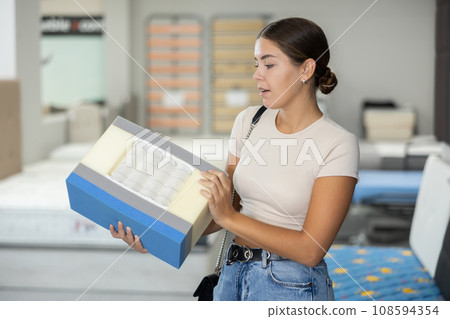 Girl examines samples structure of spring mattress in furniture store. 108594354