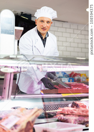 Confident male butcher slicing big piece of beef in butcher shop 108594375