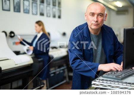 Printing house employee works on printing equipment 108594376