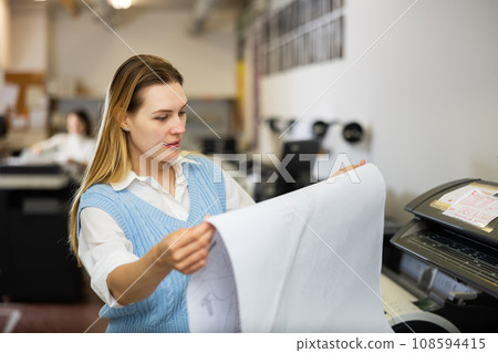 Printing establishment worker examining large piece of paper 108594415