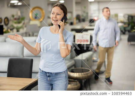 Happy female customer in furniture store talks on phone and consults with spouse about purchase 108594463