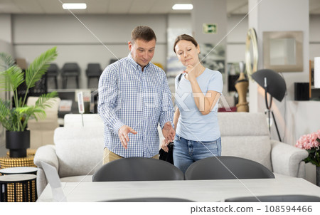 Spouses choose dining table desk in furniture store showroom Spouses choose dining table desk in furniture store showroom 108594466