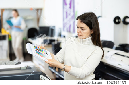 Female employee of the copy center checks the quality of the print on color chart 108594485