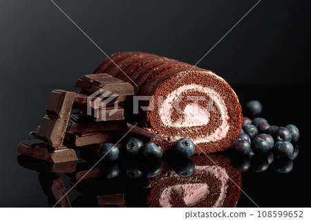 Chocolate roll cake with blueberries and a broken black chocolate bar. Chocolate roll cake with blueberries and a broken black chocolate bar. 108599652
