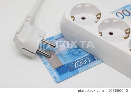 White electric cable and extension cord socket lie on a banknote, expensive electricity White electric cable and extension cord socket lie on a banknote, expensive electricity 108600640