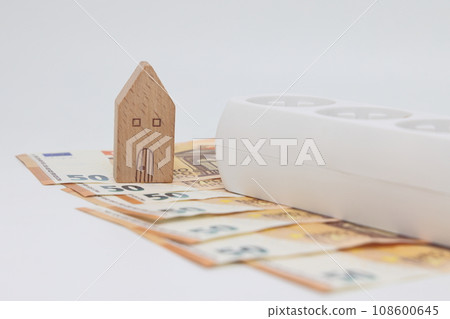 A white electric cable lies on banknotes against the backdrop of a house, expensive electricity A white electric cable lies on banknotes against the backdrop of a house, expensive electricity 108600645