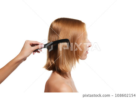 Female hand brushing blonde hair of a girl against white studio background. Taking care after hair look 108602154
