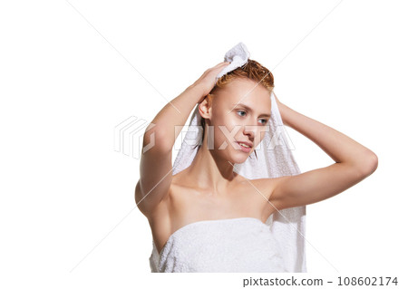 Girl standing in towel with wet hair after shower against white studio background. Drying hair with towel Girl standing in towel with wet hair after shower against white studio background. Drying hair with towel 108602174