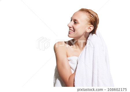 Girl standing in towel with wet hair after shower against white studio background. Drying hair with towel Girl standing in towel with wet hair after shower against white studio background. Drying hair with towel 108602175