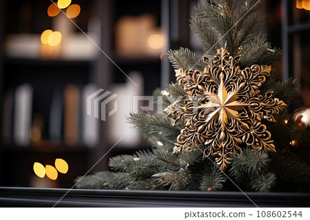 a gold snowflorer on a christmas tree in front of a bookcase with blurred lights behind it 108602544