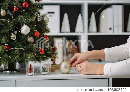 someone decorating a christmas tree with red and silver baknots on the table in front of a white bookcase someone decorating a christmas tree with red and silver baknots on the table in front of a white bookcase 108602721