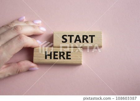 Start here symbol. Wooden blocks with words Start here Beautiful pink background. Businessman hand. Business and Start here concept. Copy space. 108603387