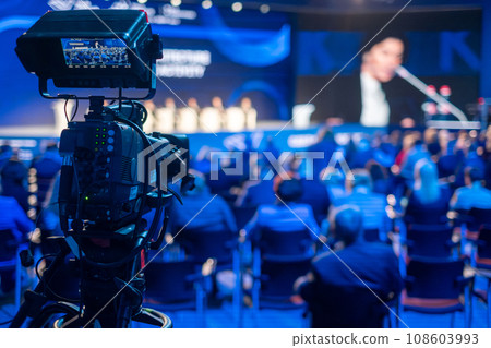Video camera capturing global business conference in illuminated blue auditorium at export forum 108603993