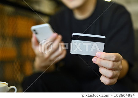 Young man holding credit card making online payment purchase or shopping online on smartphone Young man holding credit card making online payment purchase or shopping online on smartphone 108604984
