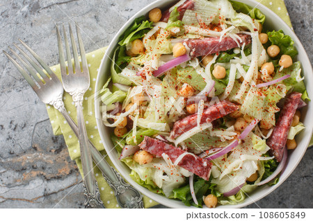 Simple salad combines salami, mozzarella, chickpeas, iceberg lettuce, and romaine, all topped off with a simple red wine vinaigrette close-up in a bowl. Horizontal top view 108605849