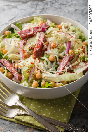 Fresh chickpea salami salad with iceberg and romaine lettuce, mozzarella, onion close-up in a bowl. Vertical 108605865