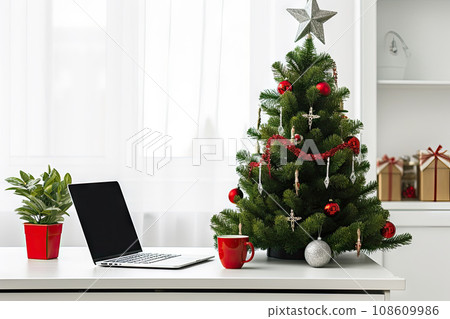 a christmas tree on a desk with a laptop and other office supplies in the fore - image is taken from above 108609986