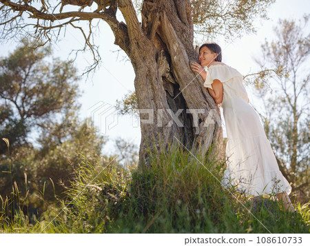 Beautiful Asian young woman in white dress outdoor near olive tree. embracing fresh air and engaging in outdoor activities. Friluftsliv concept means spending as much time outdoors as possible 108610733