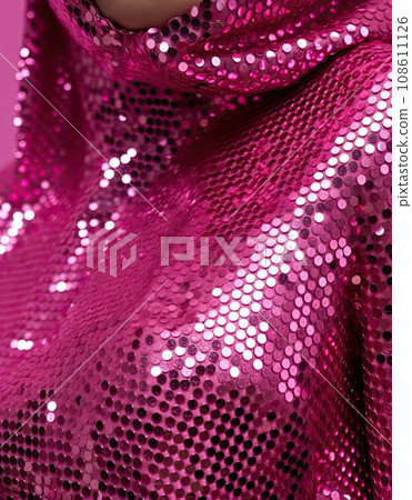 a woman wearing pink sequins and looking at the camera with her hands on her face, in front of a pink background 108611126