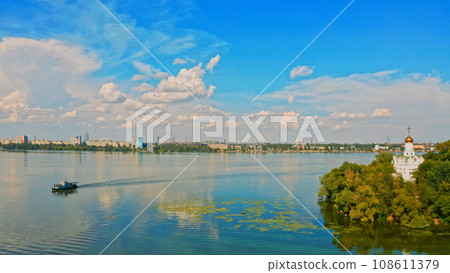 Aerial view of a floating ship on the river near the green island with a Church. Drone flying above city landscape with a river and ship... 108611379