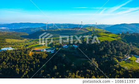 Wind farm generating green energy. Wind turbines with blades in field aerial view. Alternative energy. Scenic Aerial view of wind turbines farm over green beautiful landscape. 108611397