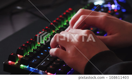 Male hands is typing on the computer keyboard, close up view. Man working on the pc computer. Human hands typing on the colourful gaming keyboard. Fingers typing on the led rgb keyboard. Male hands is typing on the computer keyboard, close up view. Man working on the pc computer. Human hands typing on the colourful gaming keyboard. Fingers typing on the led rgb keyboard. 108611403