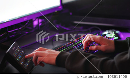 Man working on the pc computer.  Freelancer working at night on the computer. Human hands is on the table with colourful gaming keyboard and other divice. Hands pushing on the led rgb keyboard. 108611406