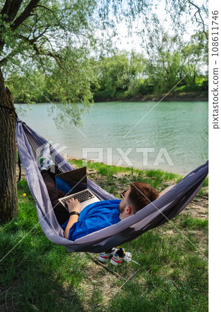 Man in Hammock with Laptop by River. Relaxing work environment Man in Hammock with Laptop by River. Relaxing work environment 108611746