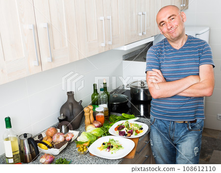 Guy stands proudly in kitchen hands clasped Guy stands proudly in kitchen hands clasped 108612110
