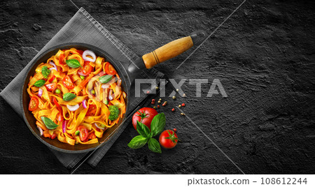 Tasty Pasta noodles linguine in tomato sauce with vegetables in pan on black stone background. 108612244