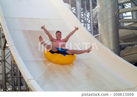 An adult man happily rides on a ring on a water slide in a water park An adult man happily rides on a ring on a water slide in a water park 108613008